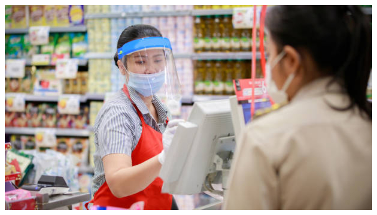 A cashier bagging a customers items. She is wearing a face mask and face shield.