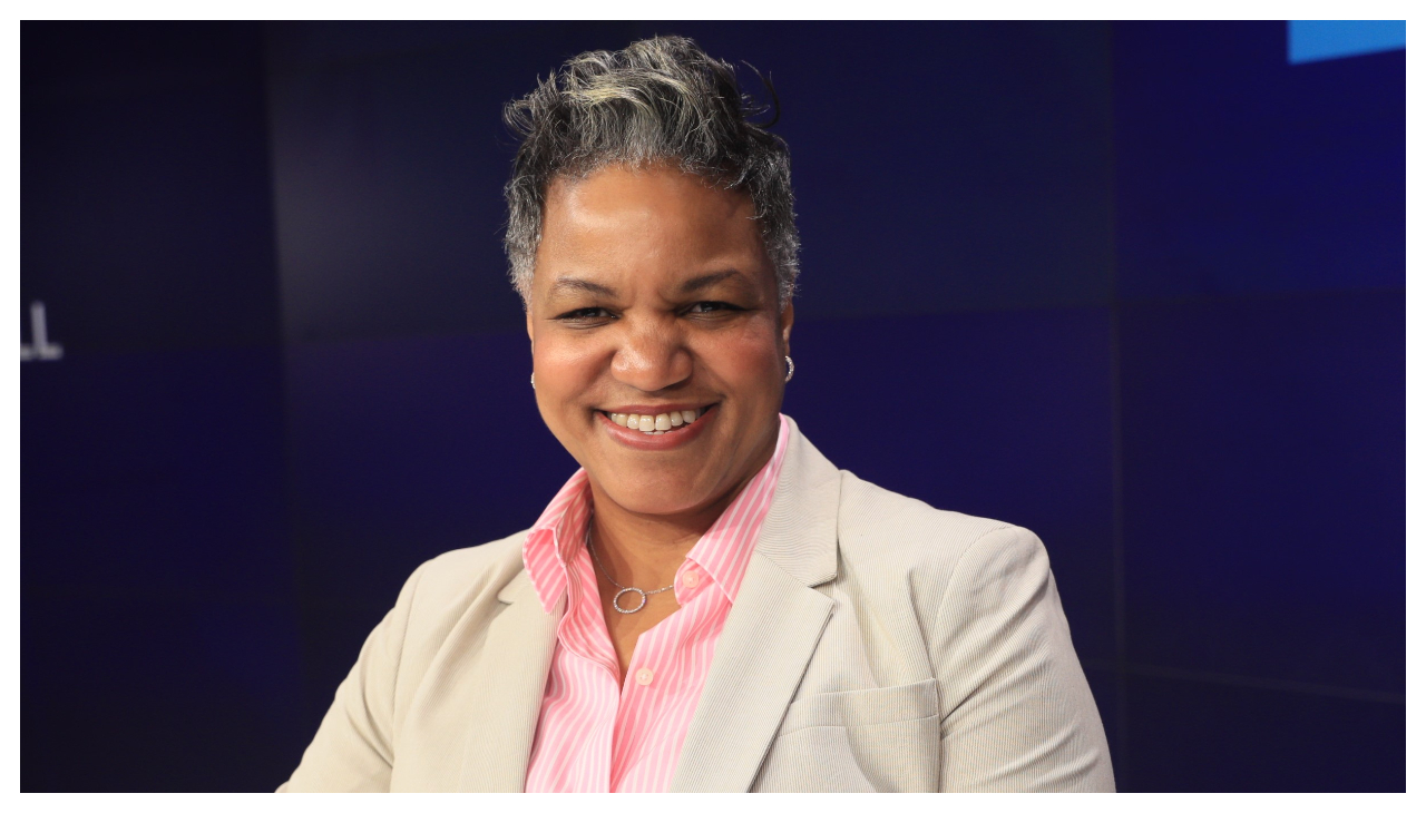 Rosanna Durruthy, an Afro-Latina woman with gray hair cut short along the sides of her head. She is wearing a cream colored suit. She is looking at the viewer and smiling.