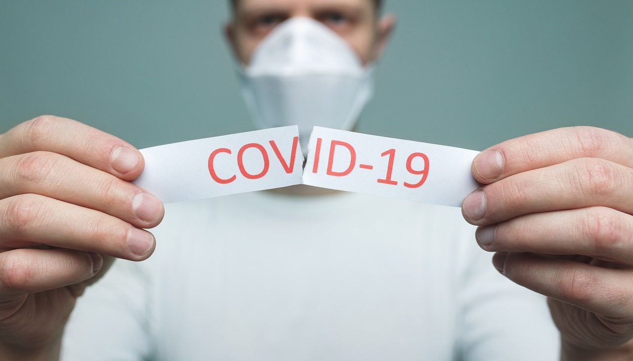 Man with a face mask breaks a piece of paper with the word COVID-19.