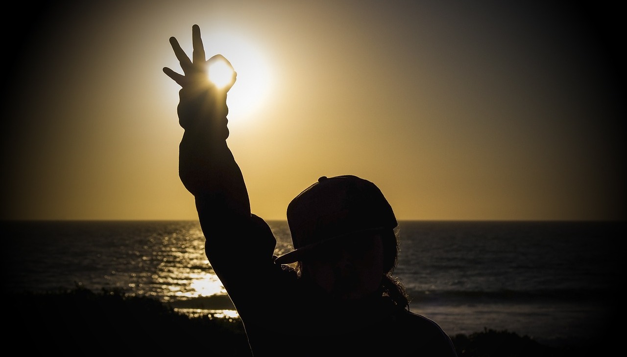 Person doing the ok sign looking to the sunset. Image to illustrate mental health. 