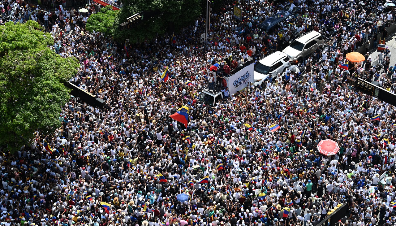 Venezuelan opposition leader Maria Corina Machado (C), waves a national flag atop a truck during a protest called by the opposition for election 'victory' to be recognised, in Caracas on August 17, 2024. (Photo by JUAN BARRETO / AFP)