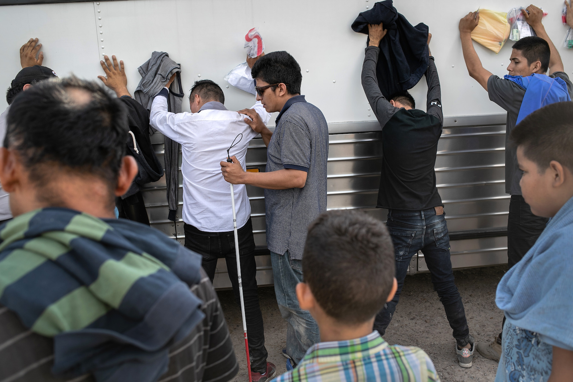 Immigrants, including a blind man from El Salvador (C), wait to be searched and then bussed to U.S. Border Patrol facility in McAllen after crossing the border from Mexico on July 02, 2019 in Los Ebanos, Texas. Photo: John Moore/Getty Images.