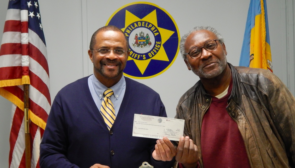 El sheriff de Filadelfia Jewell Williams (izq.) entregó un cheque a James Smith por la venta de su propiedad en la venta del sheriff.
